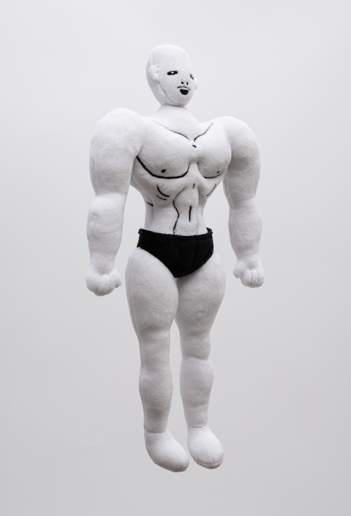 Plush figure of a muscular male character with white skin, bald head and black briefs turned at 3/4 angle against a white background.